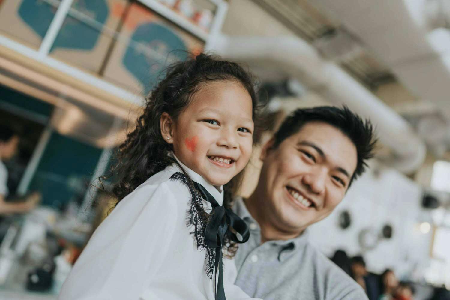 young girl smiling at camera and hugged by her dad at a birthday party