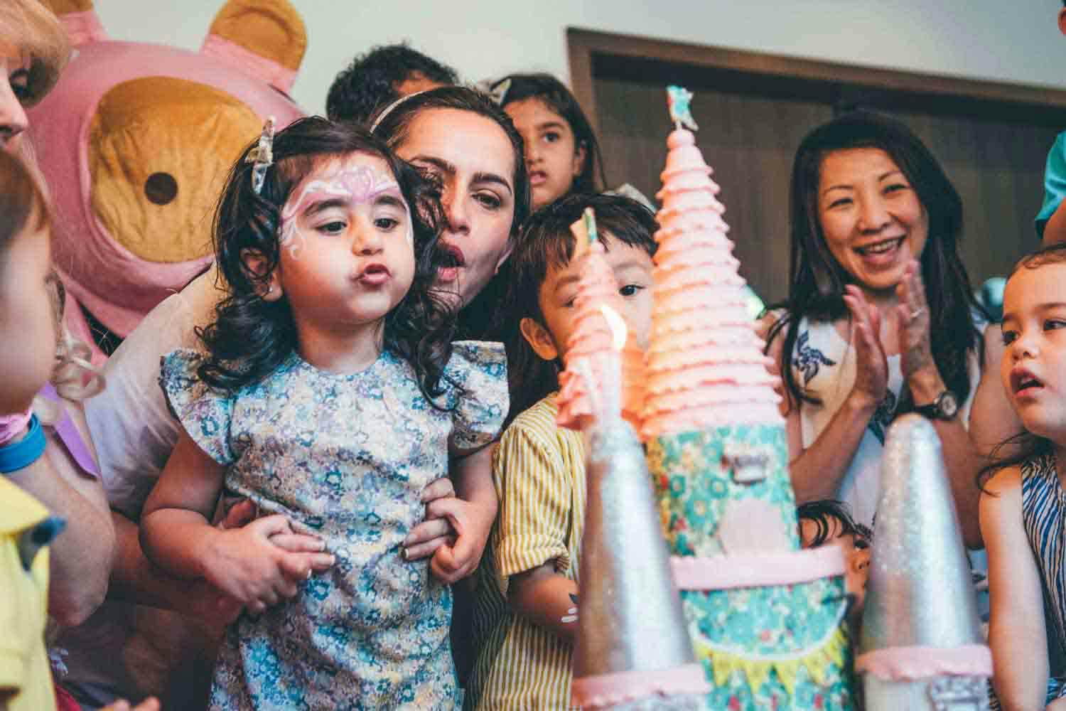 mother and daughter blowing candles on a cake together celebrating kids birthday party