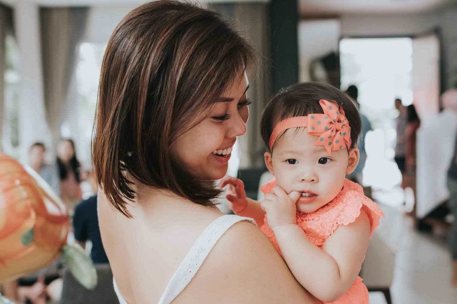 young mother smiling and looking at her daughter she is carrying in her arms during birthday party celebration event in singapore
