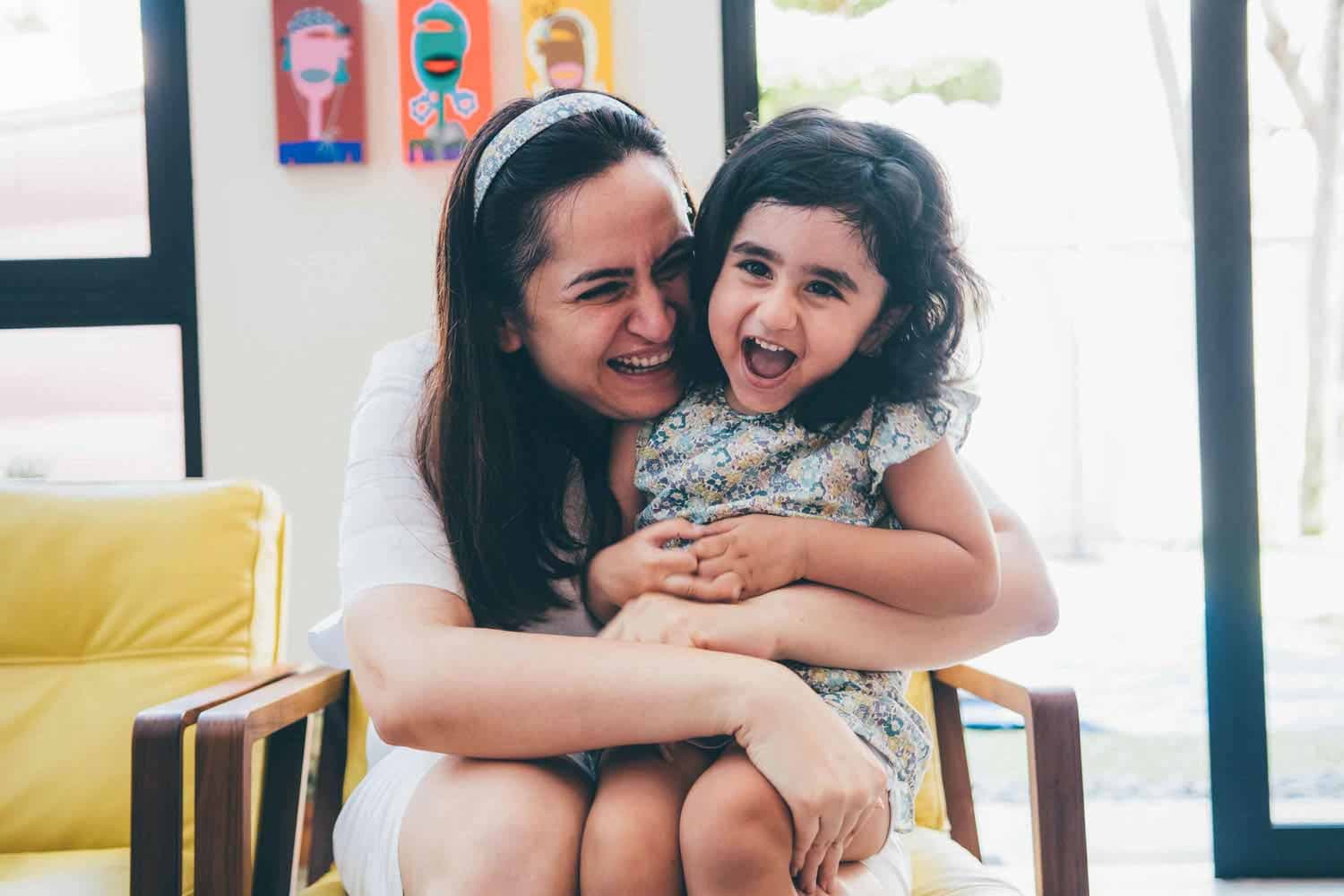 young mother hugging daughter as they laugh heartily